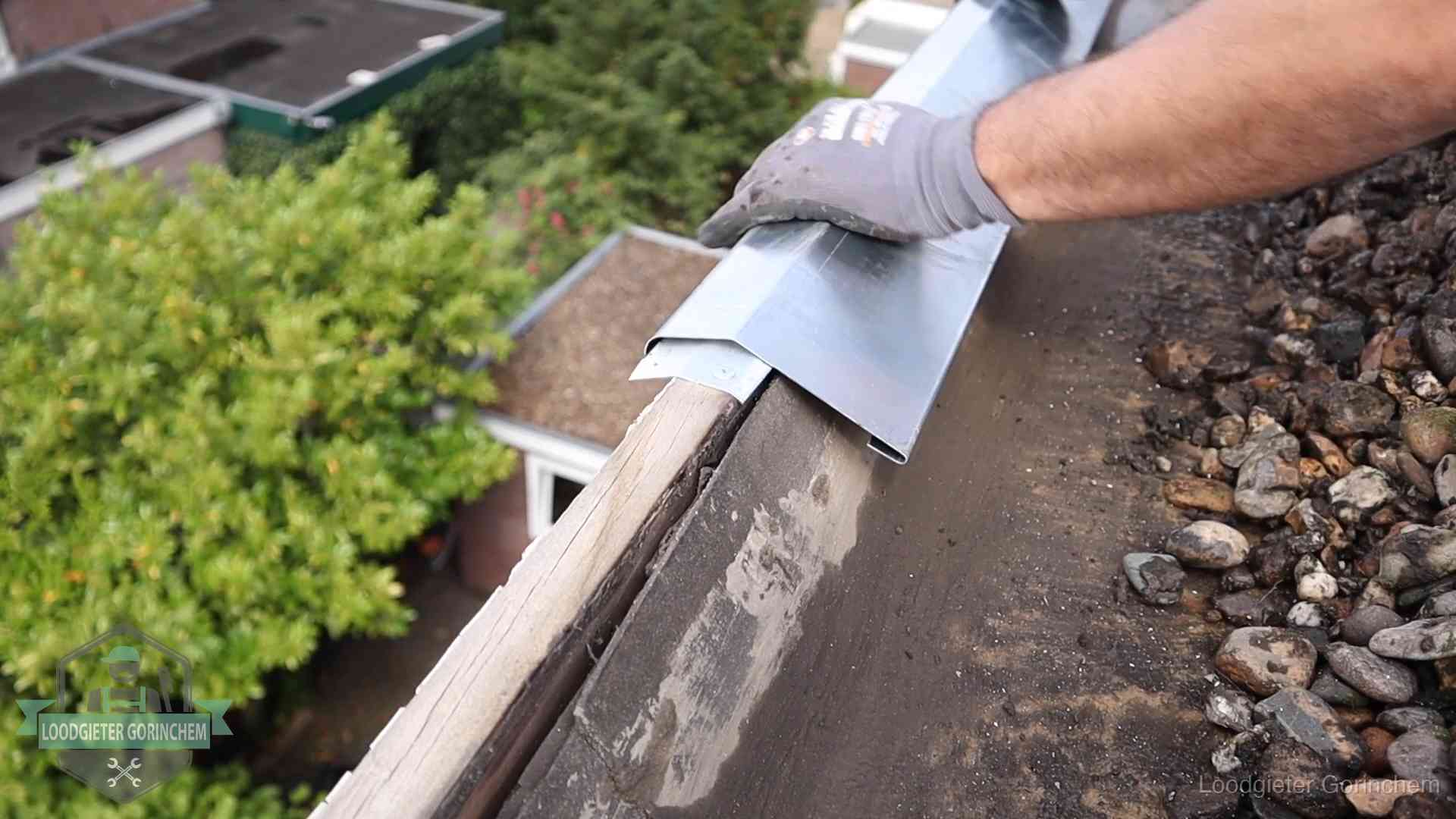Dakdekker plaatst een zinken deklijst op een dakrand met uitzicht over een woonwijk in Gorinchem