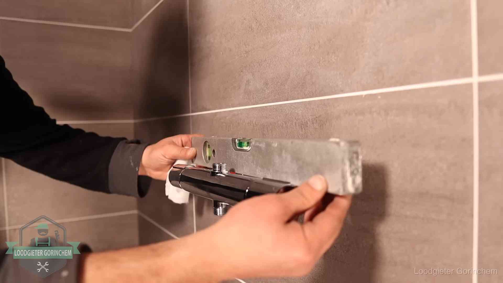 Loodgieter lijnt een douchekraan uit met een waterpas in een woning in Gorinchem